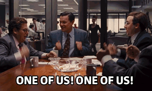 Wolf of Wallstreet GIF of businessmen sitting around a table banging their fists and chanting "One of us! One of us!"
